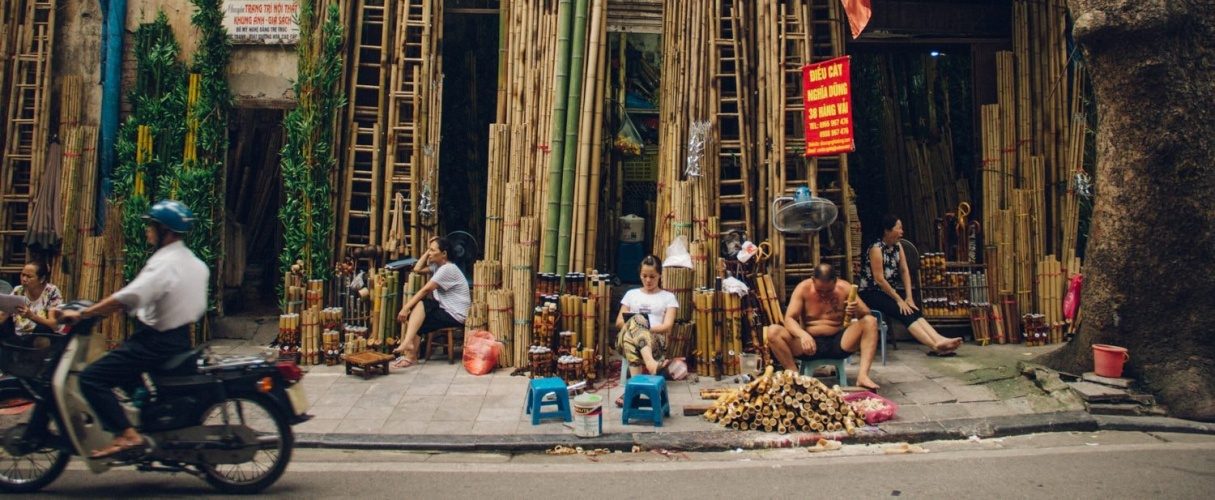 Shopfront stacked with goods on a Hanoi Old Quarter street as a motorbike passes