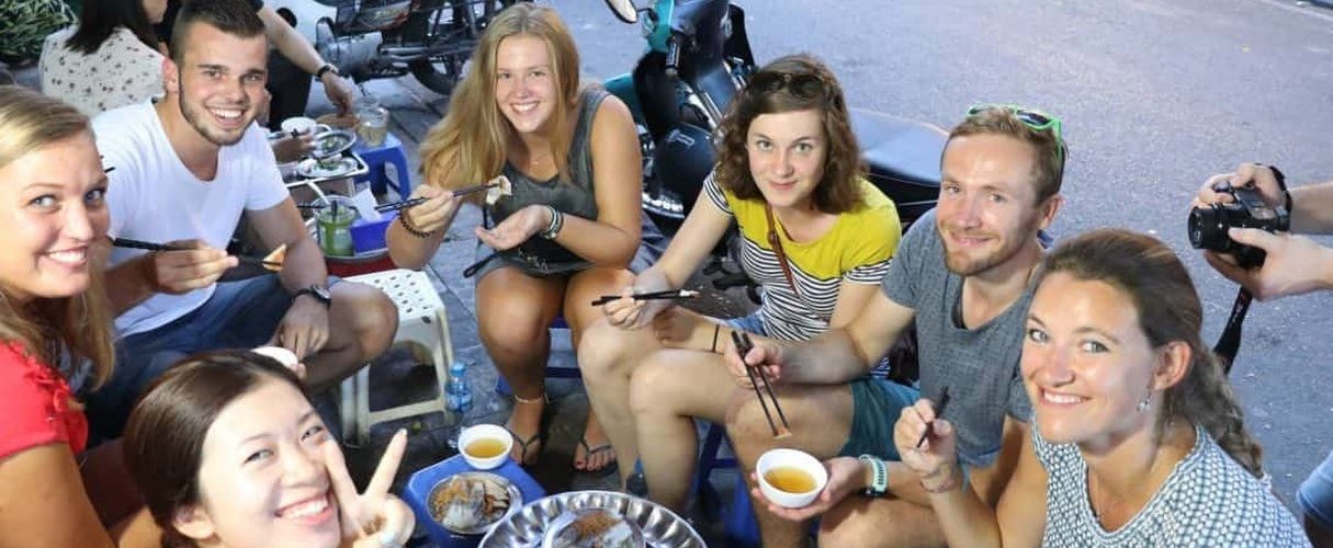 Travellers and their guides eating and drinking together on a Hanoi food tour