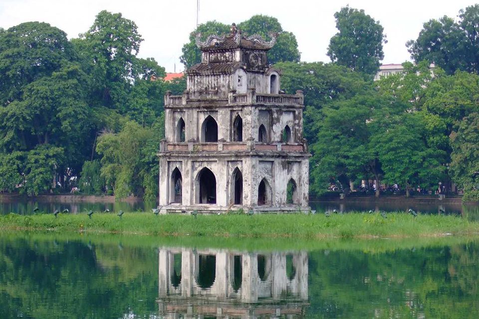 Turtle Tower reflected in the still water of Hoan Kiem Lake at midday
