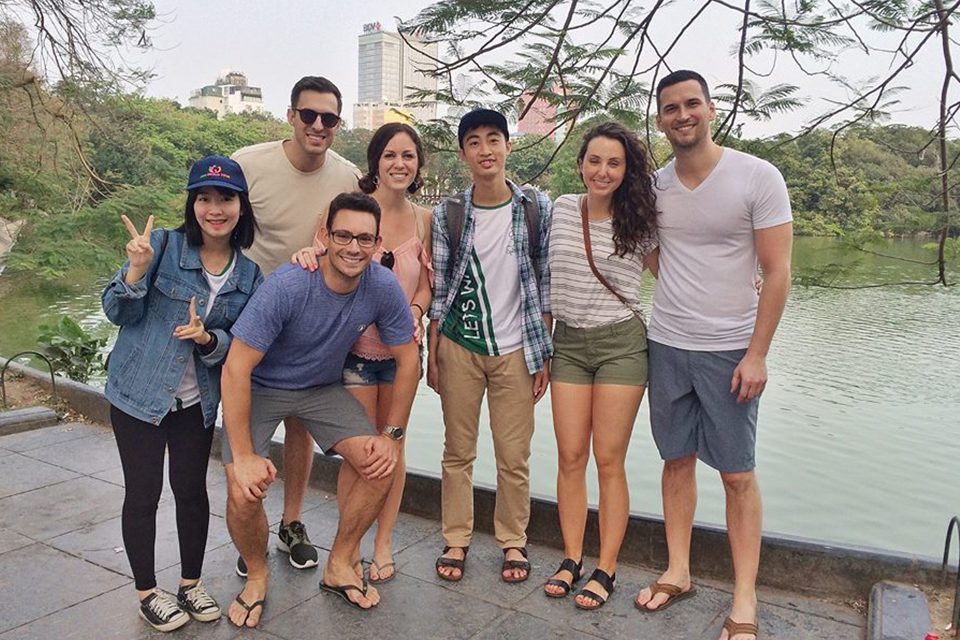 Travellers and their student guides standing together beside Hoan Kiem Lake