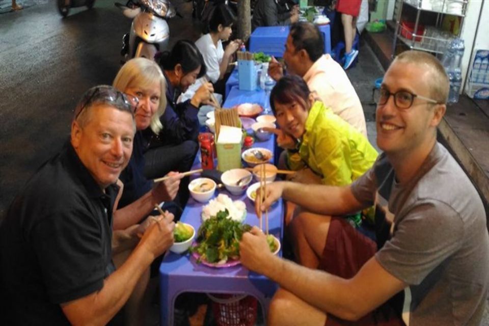 Travellers eating at a low street table on plastic stools with their guide