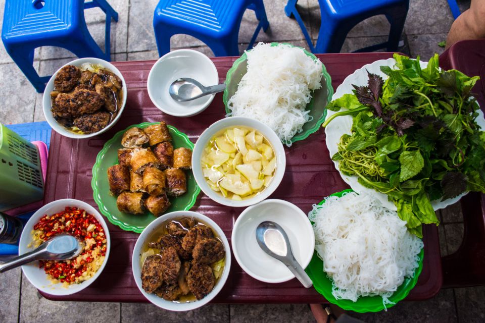 Street table spread with fried dishes, rice noodles and a plate of fresh herbs