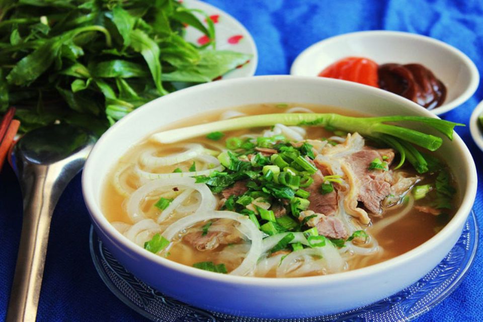 Bowl of Hanoi noodle soup topped with herbs and spring onion