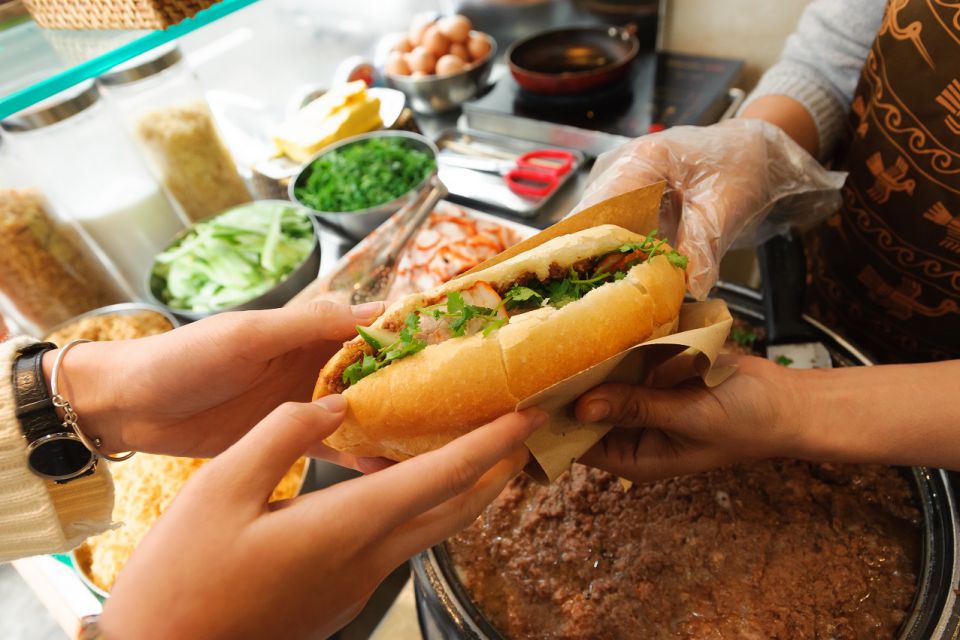 Hands filling a banh mi with pate, pork and fresh coriander at a street stall