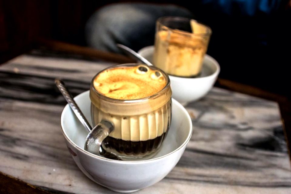 Glass of Hanoi egg coffee sitting in a bowl of hot water on a wooden table